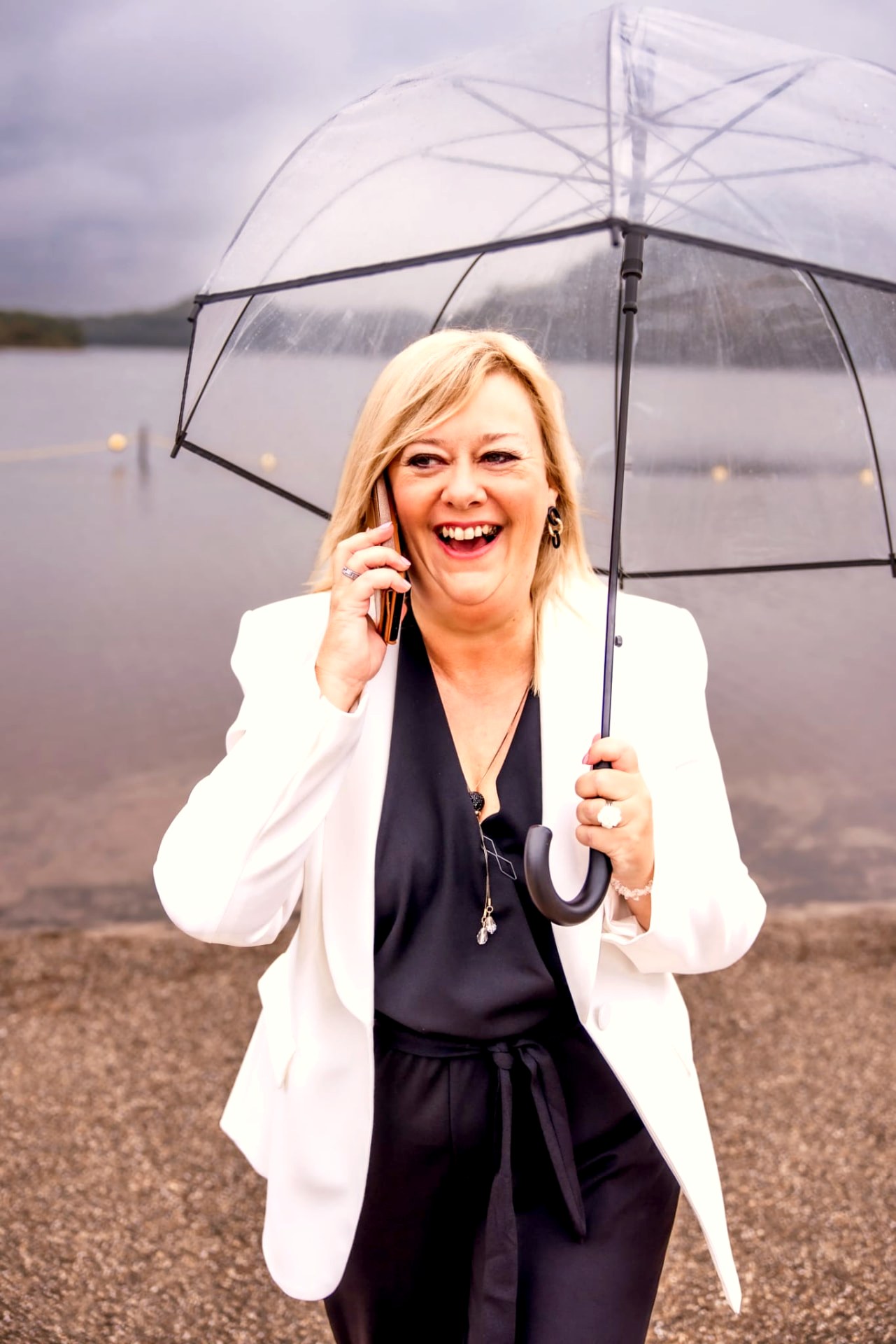 Monica Gijbels lachend met paraplu aan het water